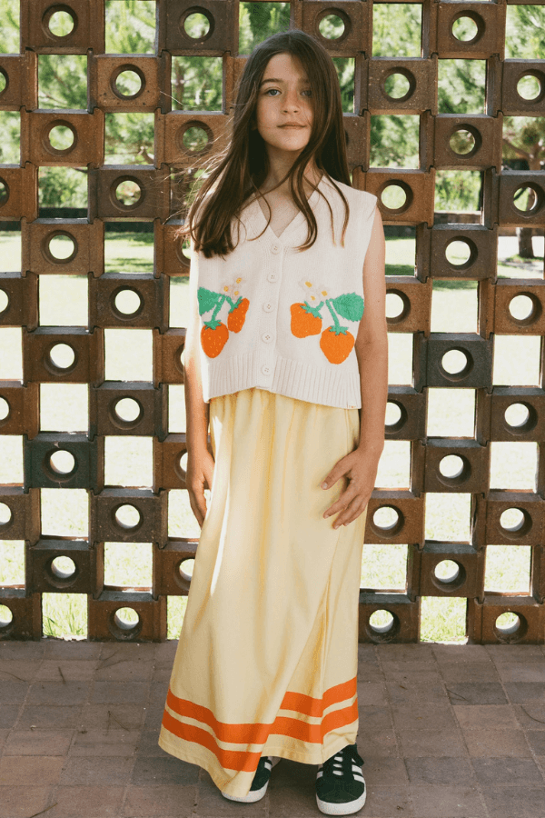 Dziewczynka z rozwianymi włosami w bolerku w truskawki i żółtej, połyskującej spódnicy. Wyprzedaż lato 2025, Tiny Cottons.