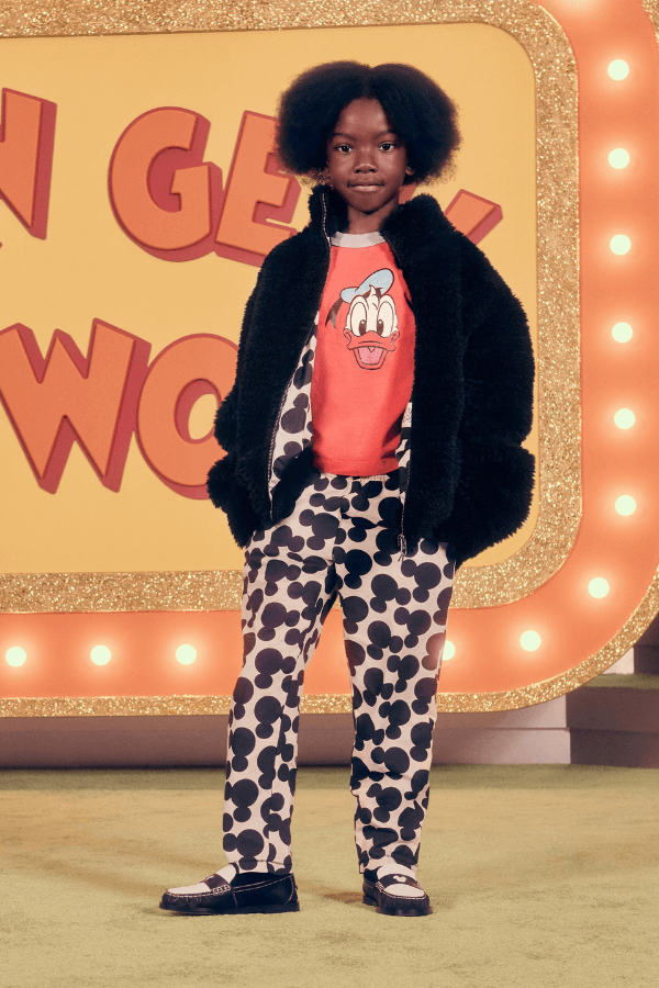 Chłopiec stoi z rękoma w kieszeniach. Ma na sobie spodnie z nadrukami w głowy Myszki Miki i koszulkę z Donaldem