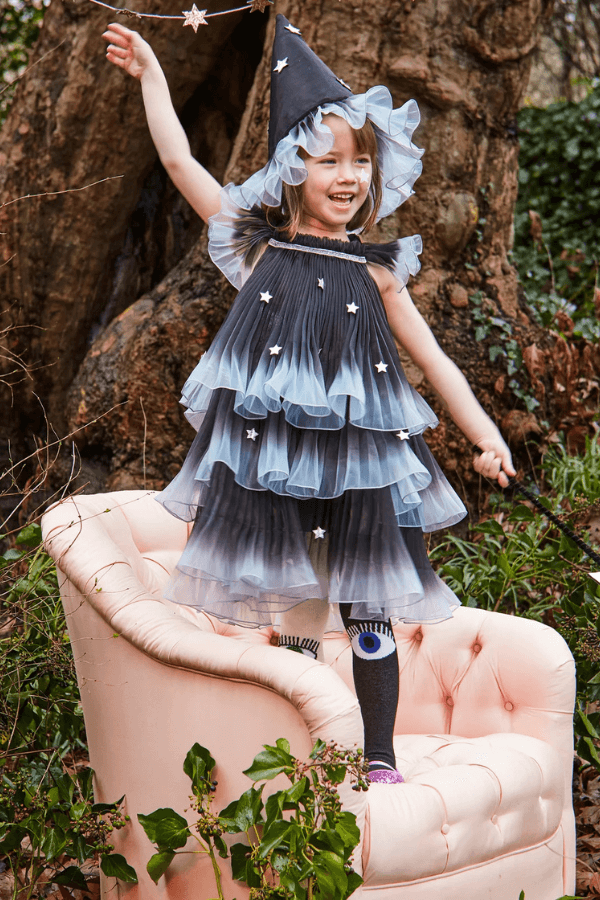 Dziewczynka w sukience w gwiazki i magicznym kapeluszu. Kostiumy na Halloween.