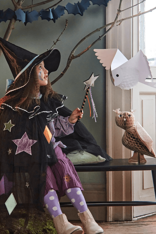 Dziewczynka w kostiumie na Halloween siedzi i patrzy w górę.