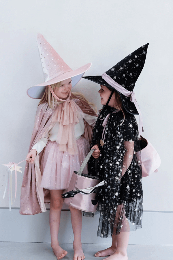 Dwie dziewczynki rozmawiają ze sobą i się śmieją. Są ubrane w halloweenowe kostiumy wiedźm.