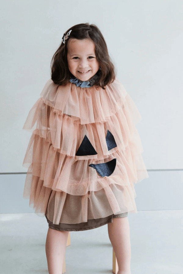 Dziewczynka stoi i uśmiecha się. Ma na sobie strój dyni.